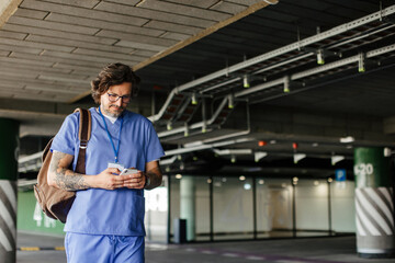 Doctor in uniform in parking lot, going home from work, texting on smartphone. Work-life balance of healthcare worker.