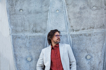 Portrait of mature businessman standing on city street, in front of office building. Handsome man with glasses in suit.