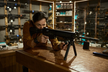 Male customer testing new model of automatic rifle in weapon store