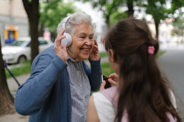 Grandma picking up young girl from school at afternoon. Granddaughter showing funny video on smartphone to senior grandmother.