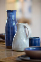 Vase bleu et cruche grise en céramique sur une table en bois, avec de la vaisselle.