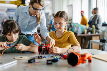 Female teacher helping to girls working on small robot, building robotic car in after-school...