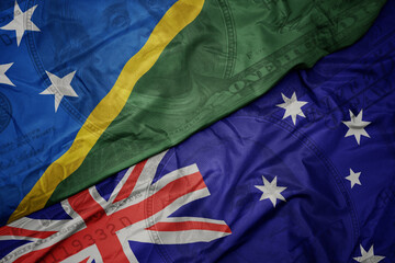 waving colorful flag of Solomon Islands and national flag of australia on the dollar money background. finance concept.