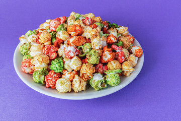 A rainbow of sweet popcorn in a plate on a purple background