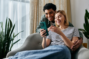 A young couple shares a laugh while looking at a smartphone in their modern living room.