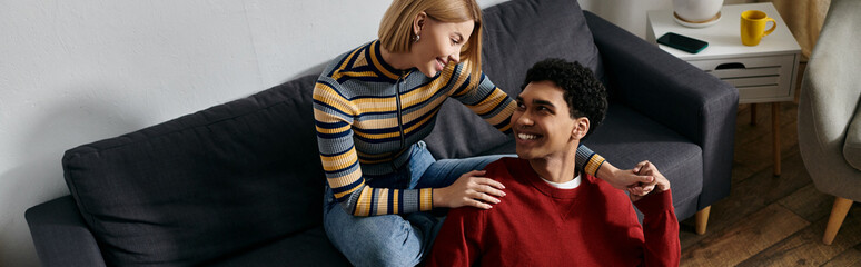 A happy, multicultural couple relaxes on a couch in their modern apartment, enjoying each others company.