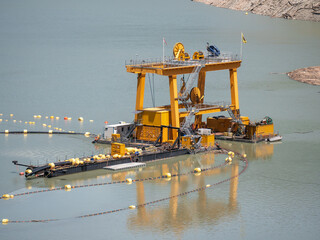 Industrial dredging machine on water used for extracting materials from riverbed or seabed. Yellow...