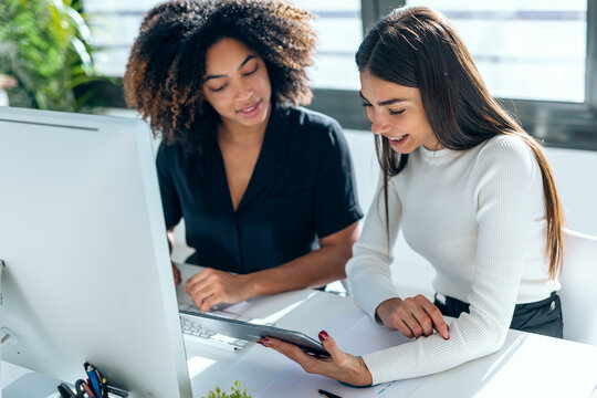 Two attractive business women talking and working with computer and digital tablet in coworking place