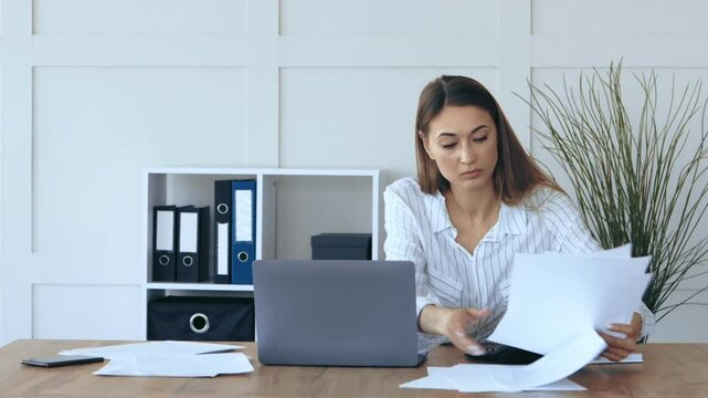 Worried business lady searching important documents or information in heap of papers on worktable in home office