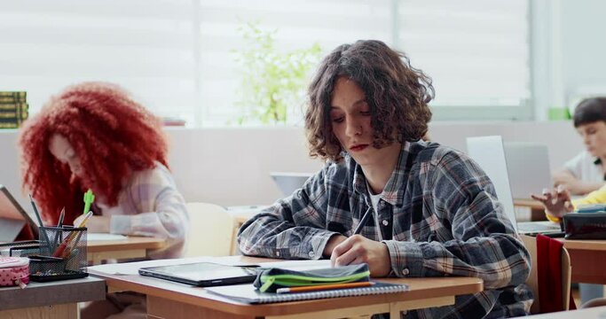 Caucasian boy studying hard during lesson. Education concept. Writing down information. Using tablet device with touch screen for additional visual images or text. Modern technology.