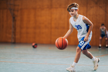 Naklejka premium Kid dribbling basketball in gym