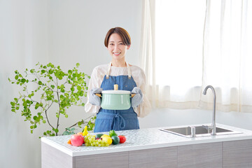 キッチンで鍋を運ぶ女性　カメラ目線