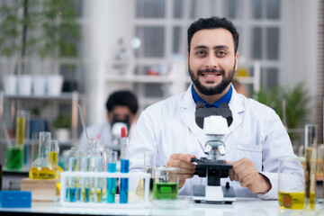 Portrait of confident medical researcher in laboratory with microscope smilling, looking at camera.
