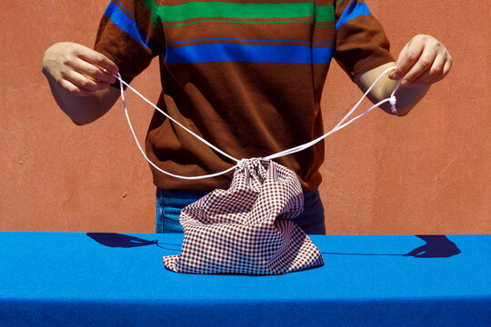Woman pulling strings of drawstring Bag on blue table