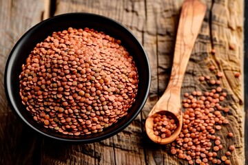 Raw red lentils in a black bowl. Wooden spoon and scattered lentils on the counter. Wooden surface
