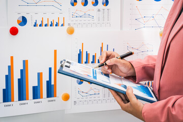 A businesswoman works diligently at her desk, reviewing financial documents and analyzing...