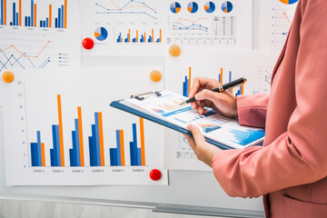 A businesswoman works diligently at her desk, reviewing financial documents and analyzing...