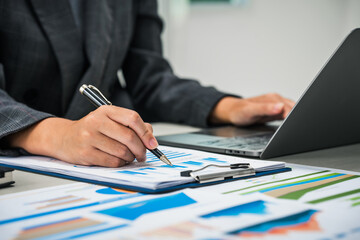 A businesswoman works diligently at her desk, reviewing financial documents and analyzing...