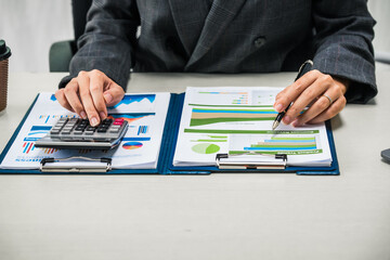 A businesswoman works diligently at her desk, reviewing financial documents and analyzing...