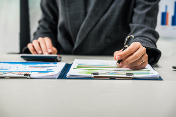 A businesswoman works diligently at her desk, reviewing financial documents and analyzing...