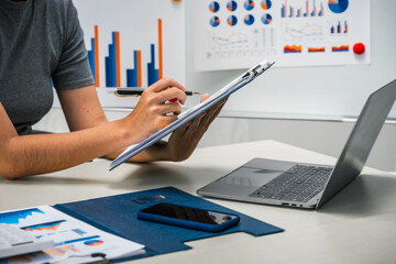 A businesswoman works diligently at her desk, reviewing financial documents and analyzing...