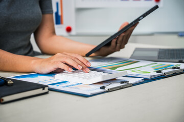 A businesswoman works diligently at her desk, reviewing financial documents and analyzing...