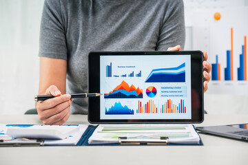 A businesswoman works diligently at her desk, reviewing financial documents and analyzing...
