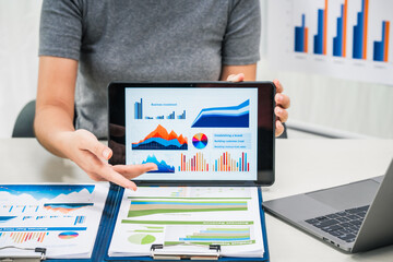 A businesswoman works diligently at her desk, reviewing financial documents and analyzing...