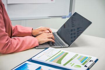 A businesswoman works diligently at her desk, reviewing financial documents and analyzing...