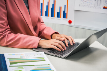 A businesswoman works diligently at her desk, reviewing financial documents and analyzing...