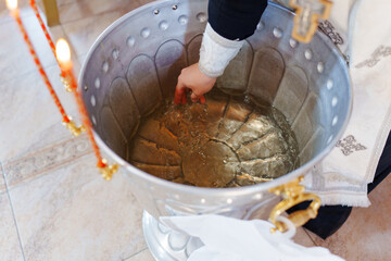 Fototapeta premium The priest's holds hand into the holy water in the baptismal font. The Sacrament of Baptism in the Orthodox Church.