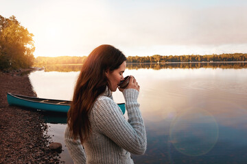 Outdoor, river and coffee to enjoy for woman, nature and sunrise in morning, thinking and break for vacation. Travel, happy or girl with tea, smile and trip in autumn, peace or countryside in Finland