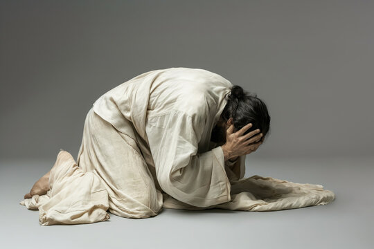 Man in white robes kneeling and holding head in hands, expressing deep emotion. Religious and spiritual background depicting prayer, faith, and introspection.