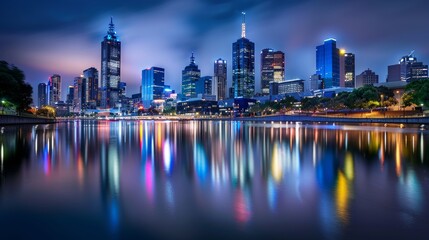 Obraz premium vibrant city skyline at night, with illuminated skyscrapers reflecting in a tranquil river below.