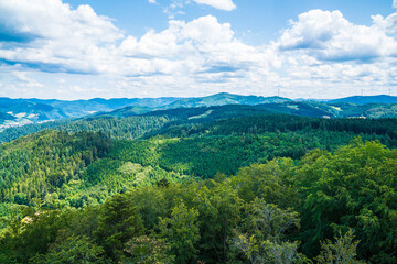 Fototapeta premium Germany, Aerial panorama nature landscape view above schwarzwald tree tops, mountains and valleys and wind turbines on sunny day