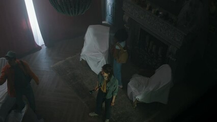 Overhead shot of three teenagers examining old abandoned mansion, using flashlight and filming content in dark