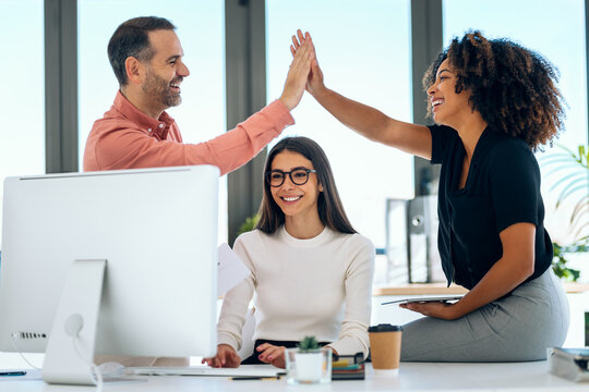 Successful business multiage team celebrating standing around table in the coworking space.
