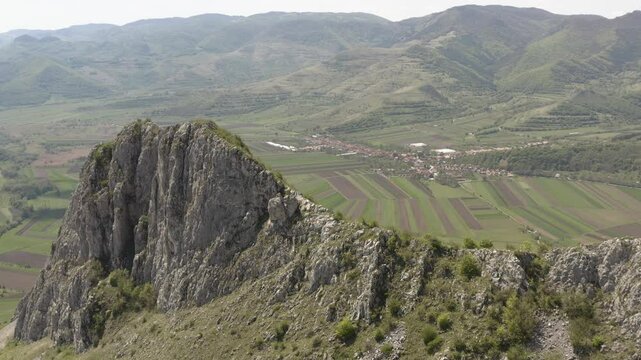 Flyover above peak of Piatra Secuiului in Romania, revealing fertile farmland in valley below, near villages of Rimetea and Pietroasa