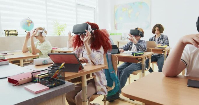 Class full of students learning about augmented reality. Children wearing VR glasses and trying to move objects with the movement of their hands. Studying other ways of teaching. Modern technology.