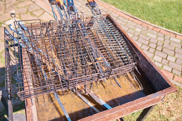 Old rusty iron brazier with iron dirty grill grate and meat skewers standing on ground near green grass in summer. Selective focus