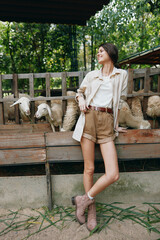 A woman standing in front of a fence with sheep in a pen next to her