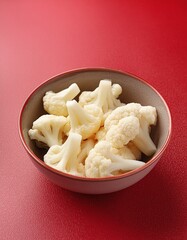 Fresh peeled cauliflower in bowl on red background