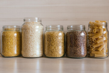 Buckwheat, pasta, bulgur and rice in glass jars on a wooden table. 