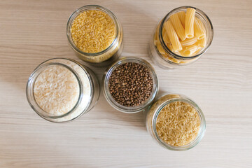 Buckwheat, pasta, bulgur and rice in glass jars on a wooden table. View from above.