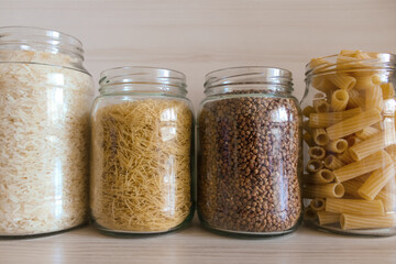 A row of glass jars filled with various types of food.  Buckwheat, pasta, bulgur and rice in glass...