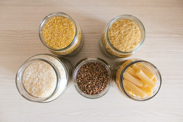 Buckwheat, pasta, bulgur and rice in glass jars on a wooden table. View from above.
