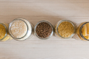 Buckwheat, pasta, bulgur and rice in glass jars on a wooden table. View from above.