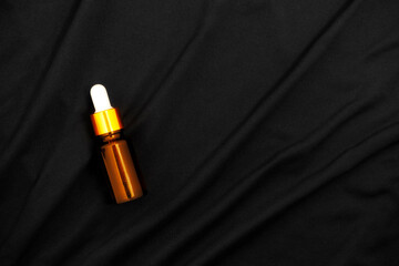 Naklejka premium Dropper bottle on black fabric texture background. Serum bottle for mockup.