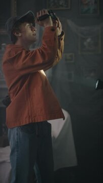 Vertical medium long shot of curious Caucasian boy recording video on vhs camera while diverse girl friends exploring interior of old abandoned house with sheet covered furniture using flashlights