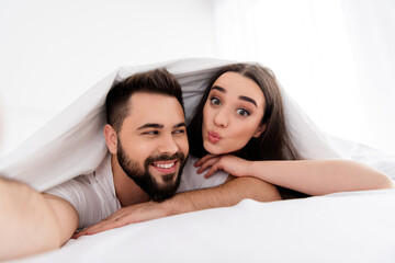 Photo of flirty funny boyfriend girlfriend sleepwear tacking selfie sending kiss indoors home bedroom